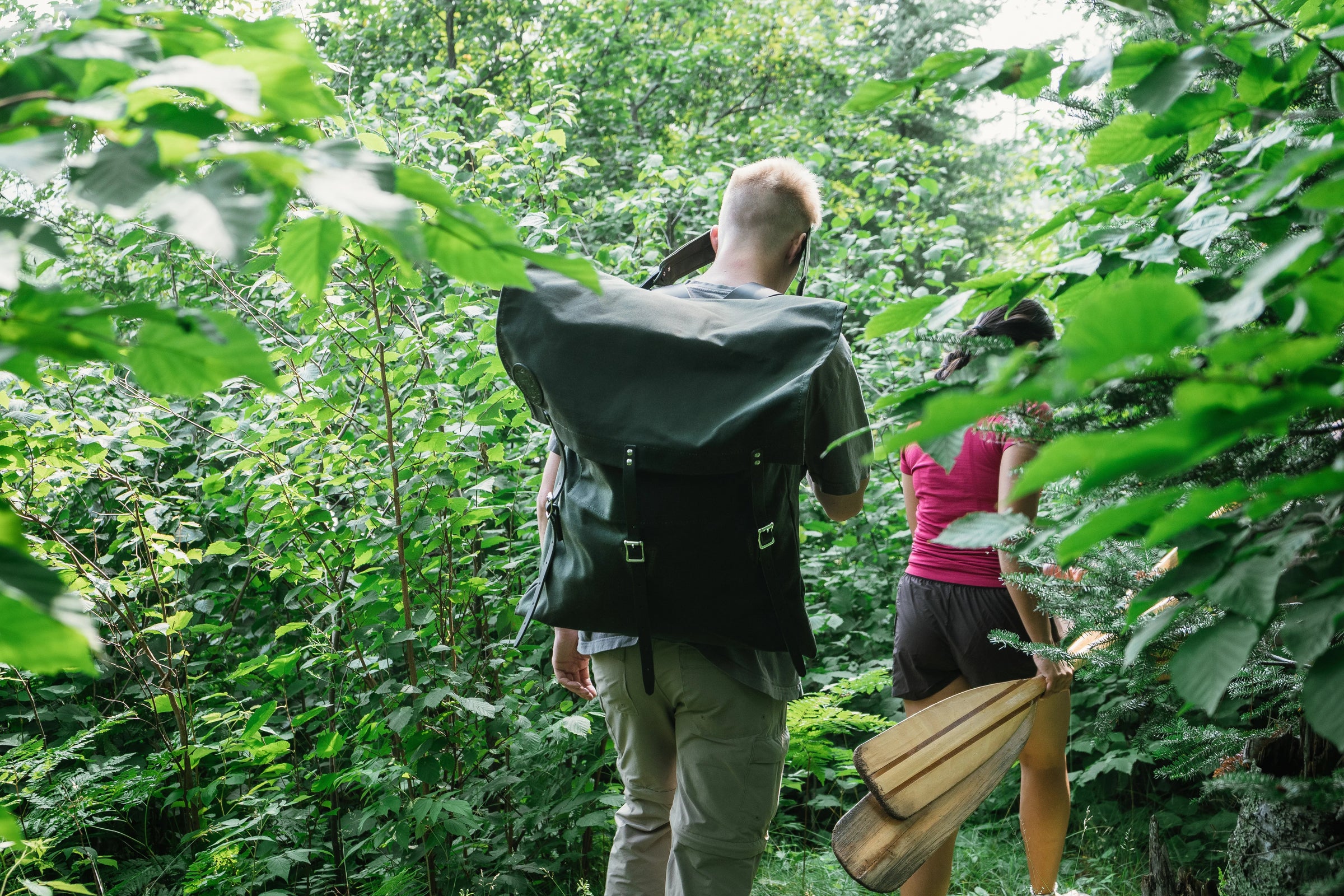 Man wearing a Duluth Pack Canoe Pack walking with a woman holding a canoe paddle in the forest. 