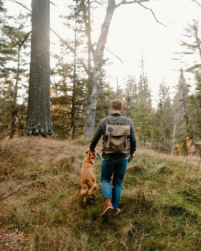 DOODLE BAG CHARM (PDP Test) in rugged canvas and leather, featured on a man hiking through a forest trail with his dog, highlighting outdoor heritage by DOUGLAS COMPANY, INC.