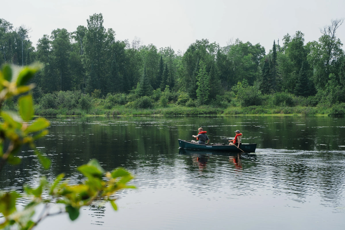 Photo: A man and woman canoeing on a clear lake. They are surrounded by a green forest. 