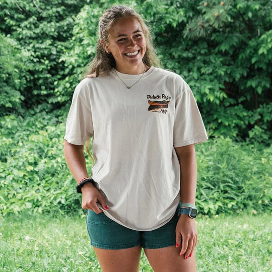 Duluth Pack Canoe Adventure T-Shirt in cappuccino color worn outdoors, featuring soft cotton fabric with Northern Minnesota canoe graphics by LAKESHIRTS, INC.
