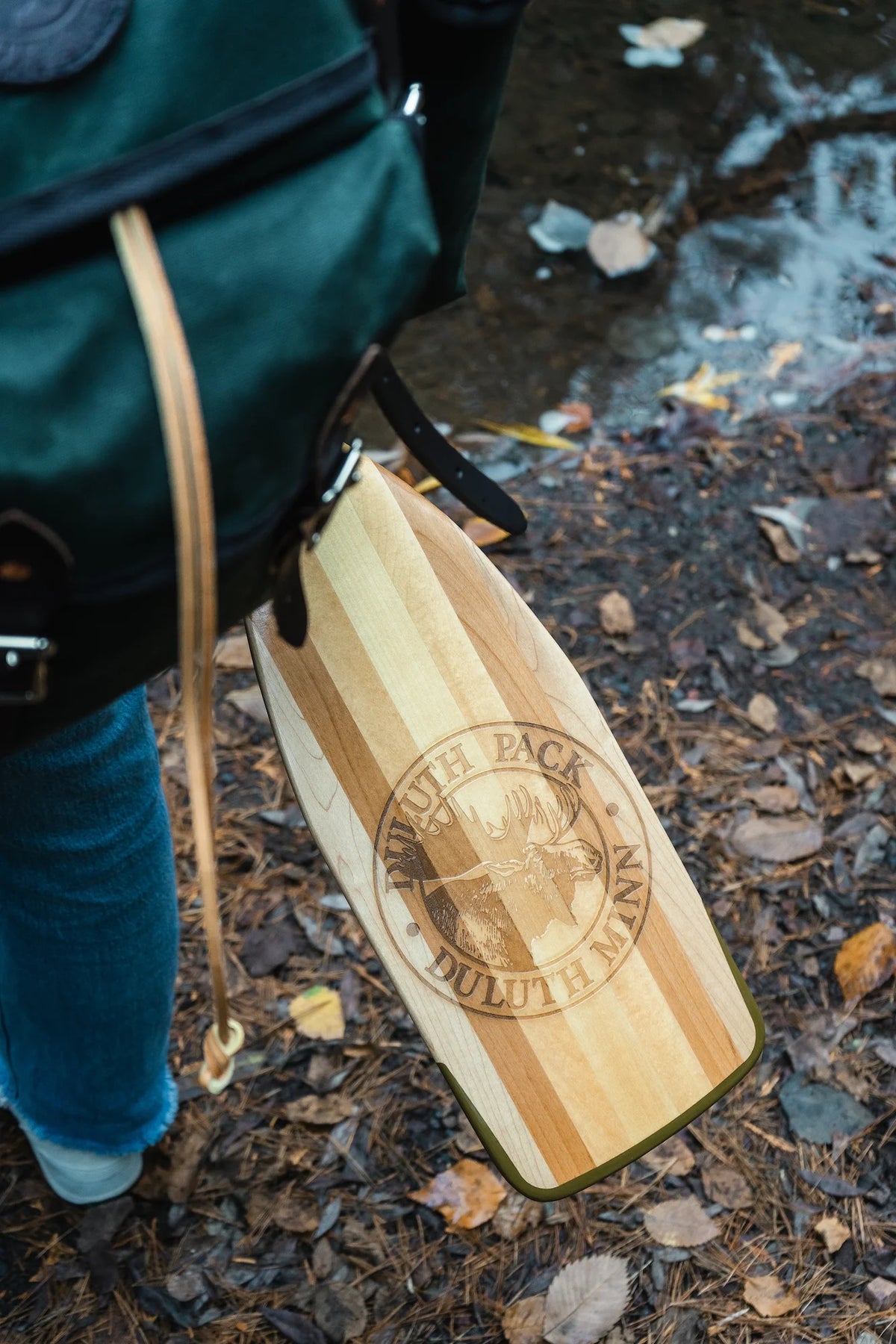 An image of a products won in the Outdoorsman's Giveaway. Win a Duluth Pack Gitchi Gami Wanderer hiking backpack with a Bending Branches BB Special 11 Canoe Paddle and a pair of Loyak barefoot Astral shoes. The products are cedar tree roots with a waterfall in the background.